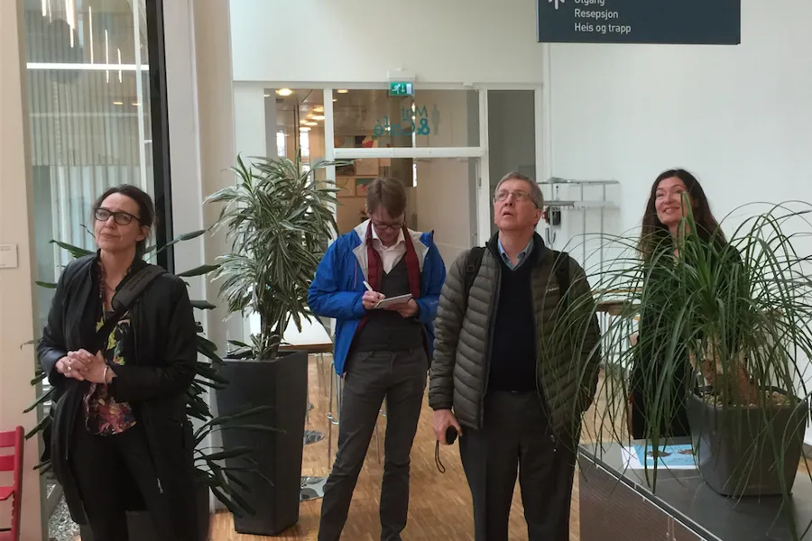 En gruppe mennesker som står i et rom med planter og et skilt